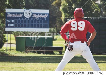 A baseball player on the pitch standing with his back towards the camera with an empty scoreboard in the background 100705768