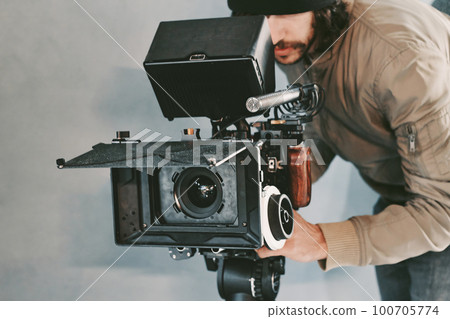 A young male cameraman behind a movie video camera filming on set 100705774