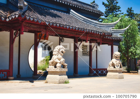 Entrance to a Chinese garden with two stone lions and a circular doorway 100705790