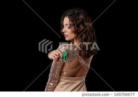 Brunette girl wearing shiny dress posing holding some chips in her hand standing against black studio background. Casino, poker. Close-up. Brunette girl wearing shiny dress posing holding some chips in her hand standing against black studio background. Casino, poker. Close-up. 100706677