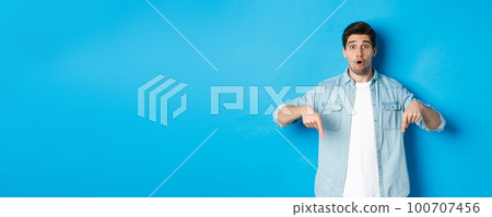 Surprised bearded adult man in casual outfit, pointing fingers down and looking startled, asking question about promotion, standing over blue background Surprised bearded adult man in casual outfit, pointing fingers down and looking startled, asking question about promotion, standing over blue background 100707456