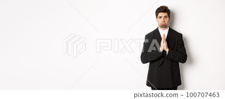 Miserable clingy guy need help, pouting silly and begging for something, asking for favour, standing against white background in black suit Miserable clingy guy need help, pouting silly and begging for something, asking for favour, standing against white background in black suit 100707463