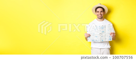 Travelling, vacation and tourism concept. Smiling young man going on trip, holding road map and smiling, standing over yellow background Travelling, vacation and tourism concept. Smiling young man going on trip, holding road map and smiling, standing over yellow background 100707556