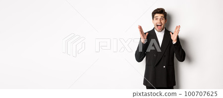 Portrait of surprised handsome businessman in suit, reacting to holidays promo, looking amazed at camera, standing over white background 100707625