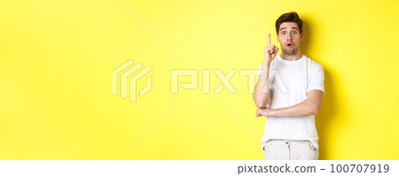 Thoughtful guy suggesting solution, raising finger in eureka sign and looking excited, have an idea, standing against yellow background 100707919