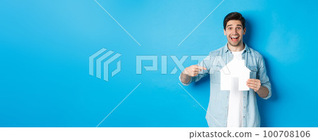 Insurance, mortgage and real estate concept. Surprised man pointing at house model and smiling, searching apartment to rent or buy, standing against blue background 100708106