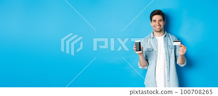 Young smiling man showing smartphone screen and credit card, concept of online shopping or banking Young smiling man showing smartphone screen and credit card, concept of online shopping or banking 100708265