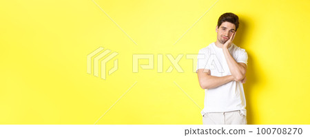 Bored and unamused man looking with indifference, standing in white clothes over yellow background Bored and unamused man looking with indifference, standing in white clothes over yellow background 100708270