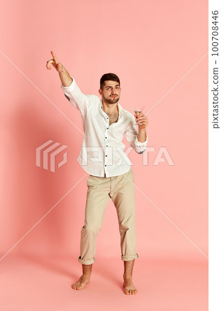Portrait of handsome young man in stylish clothes posing with cocktail, dancing against pink studio background 100708446