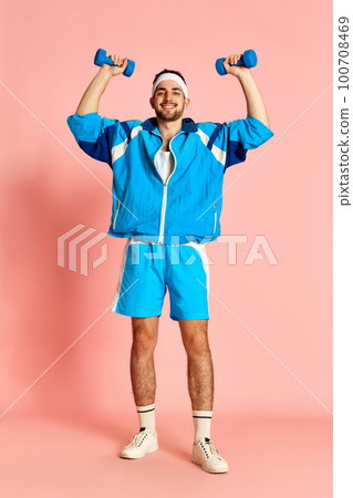 Full-length portrait of young handsome man in sportive clothes posing with dumbbells against pink studio background. Concept of sportive lifestyle 100708469