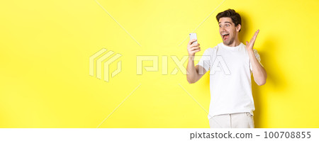 Surprised and happy man looking at mobile phone screen, reading fantastic news, standing over yellow background Surprised and happy man looking at mobile phone screen, reading fantastic news, standing over yellow background 100708855