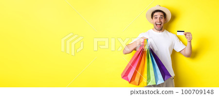 Happy guy going shopping on vacation, holding paper bags and showing credit card, standing over yellow background Happy guy going shopping on vacation, holding paper bags and showing credit card, standing over yellow background 100709148