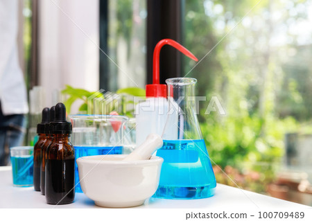 Mortar with pestle and blue experiment water in beaker and flask in chemistry science laboratory. Group of laboratory flasks with liquid inside. Mortar with pestle and blue experiment water in beaker and flask in chemistry science laboratory. Group of laboratory flasks with liquid inside. 100709489