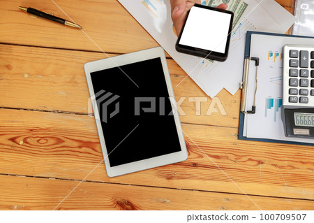 Top view of Office workspace with blank screen tablet, calculator, document and businessman using smart phone. Top view of Office workspace with blank screen tablet, calculator, document and businessman using smart phone. 100709507