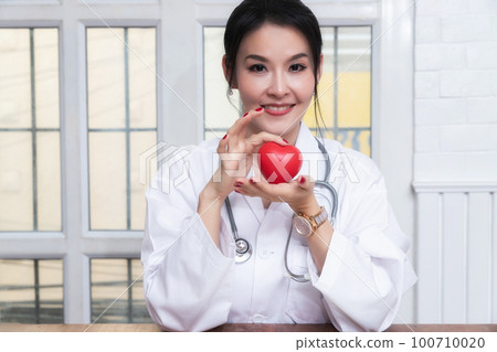 Female doctor holding a red heart ball in the hospital. Concept of health care and medical. Female doctor holding a red heart ball in the hospital. Concept of health care and medical. 100710020
