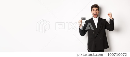 Portrait of excited handsome businessman in suit, rejoicing and showing credit card, standing against white background Portrait of excited handsome businessman in suit, rejoicing and showing credit card, standing against white background 100710072