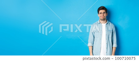 Skeptical and doubtful guy in glasses, looking confused at something strange, blue background Skeptical and doubtful guy in glasses, looking confused at something strange, blue background 100710075