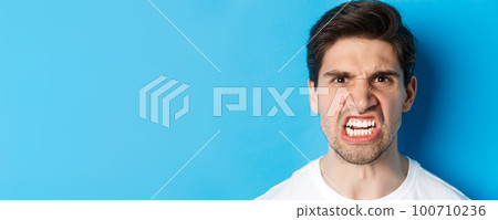 Headshot of angry caucasian man looking with scorn and dismay, being mad at person, standing against blue background 100710236