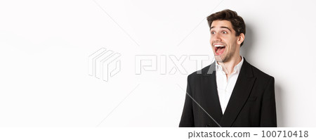 Close-up of handsome male entrepreneur in suit, looking left and smiling amazed, standing against white background Close-up of handsome male entrepreneur in suit, looking left and smiling amazed, standing against white background 100710418