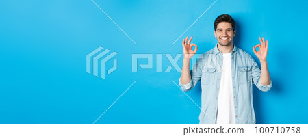 Confident smiling adult man, showing ok signs and looking pleased, like something, standing against blue background 100710758