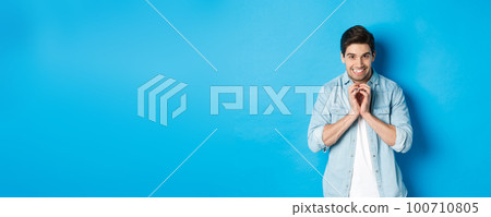 Funny cunning man having evil plan, scheming something and smiling devious, standing against blue background 100710805