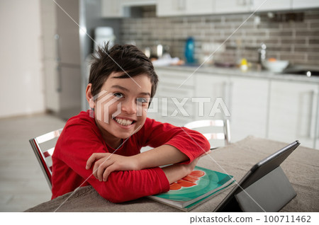 Adorable Caucasian teenage schoolboy, smart elementary age student enjoys distance learning, smiling looking at camera. Homeschooling and e-learning concept. Children. Knowledge and education 100711462
