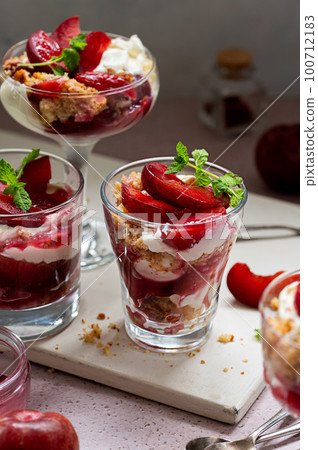 Trifles in layers with red plums and whipped cream in portioned glasses. Trifles in layers with red plums and whipped cream in portioned glasses. 100712183