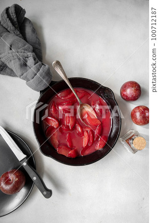 Red plums confiture or jam. Cooking fresh fruit sauce in black pan. Red plums confiture or jam. Cooking fresh fruit sauce in black pan. 100712187
