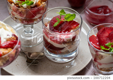 Trifles in layers with red plums and whipped cream in dessert, portioned glasses. 100712204