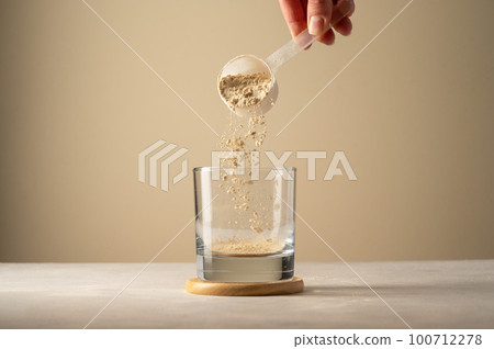 Pouring protein powder from scoop, in glass a glass. Making protein drink. Pouring protein powder from scoop, in glass a glass. Making protein drink. 100712278