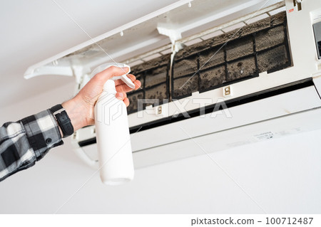 A man's hand sprays a cleaning liquid on the moldy filters of an air conditioner. 100712487
