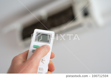 A man's hand holds a remote control from an air conditioner with a temperature on the screen of 21. A man's hand holds a remote control from an air conditioner with a temperature on the screen of 21. 100712504