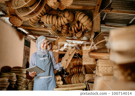 muslim woman at her bamboo products shop holding tablet pc 100714014