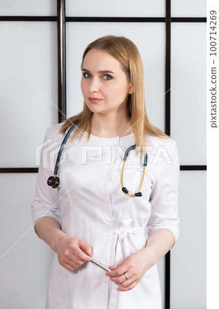 Portrait of a young woman doctor in a white uniform with a stethoscope around her neck. Family doctor, cardiologist or nurse Portrait of a young woman doctor in a white uniform with a stethoscope around her neck. Family doctor, cardiologist or nurse 100714269