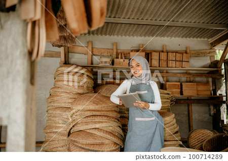 muslim woman at her bamboo products shop holding tablet pc 100714289