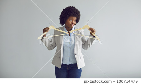 Young african american woman holding two empty hangers isolated on a gray background. 100714479