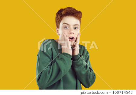 Portrait of preteen boy who is funny scared and grabs his face on orange background. Portrait of preteen boy who is funny scared and grabs his face on orange background. 100714543