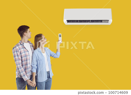 Young couple use remote control to switch air conditioner isolated on yellow background 100714609