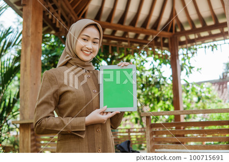 asian female teacher in hijab showing screen of a tablet 100715691