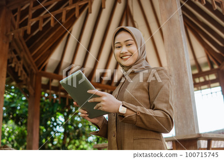 teacher in hijab smiles at camera while using a tablet 100715745