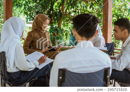 The teacher in the hijab teaches students in the gazebo The teacher in the hijab teaches students in the gazebo 100715820