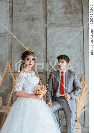 asian groom touch his suit while sitting behind the beautiful bride 100715866
