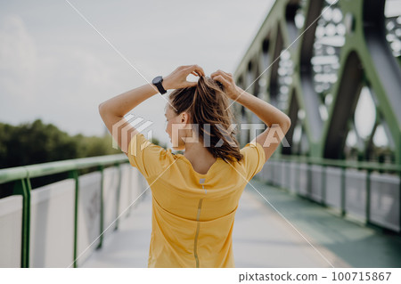 Rear view of young woman preparing for run in a city. 100715867