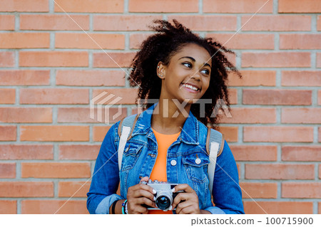 Multiracial girl standing in front of brick wall with camera, and posing. 100715900