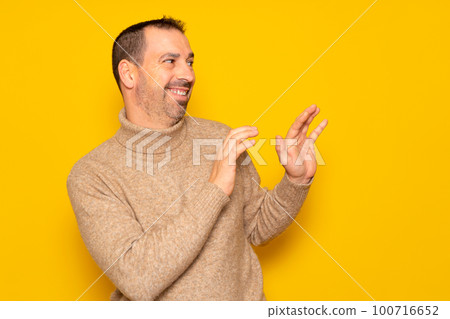 Bearded hispanic man in a turtleneck ducking to the side in embarrassment, tries to push away from something or someone with his hands. Isolated on yellow background. Bearded hispanic man in a turtleneck ducking to the side in embarrassment, tries to push away from something or someone with his hands. Isolated on yellow background. 100716652