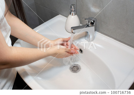 Young beautiful woman washes her hands with soap in the bathroom, toilet. Regular hand washing for hygiene. Young beautiful woman washes her hands with soap in the bathroom, toilet. Regular hand washing for hygiene. 100716736