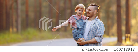 Dad and his daughter are walking along a forest road among tall pines. Dad and his daughter are walking along a forest road among tall pines. 100718918
