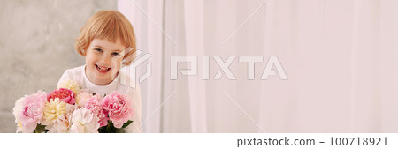 Girl 6-7 years old in a white dress holds a flower 100718921