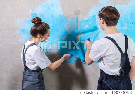 House decoration DIY renovation concept. Happy couple in empty room of new home painting wall together. Husband and wife holding paint roller painting wall with blue color paint in new house House decoration DIY renovation concept. Happy couple in empty room of new home painting wall together. Husband and wife holding paint roller painting wall with blue color paint in new house 100720798