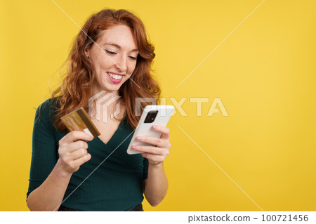 Happy redheaded woman shopping online with the mobile Happy redheaded woman shopping online with the mobile 100721456